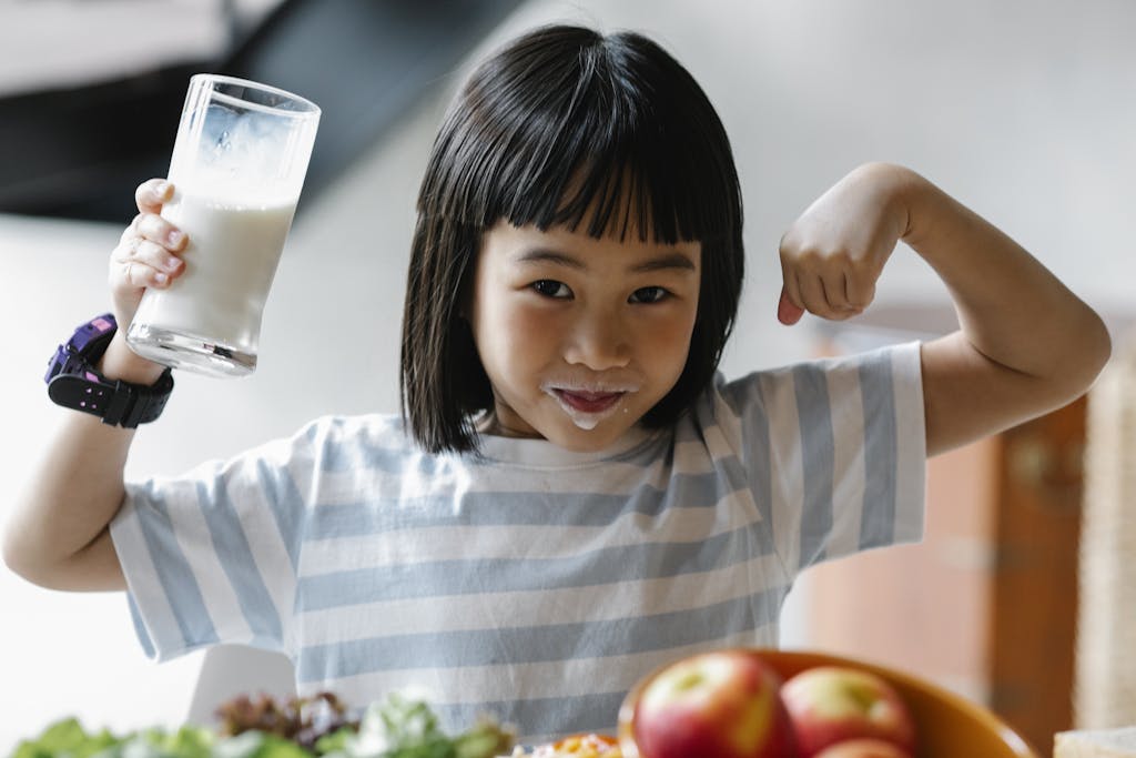 A happy child drinking milk and flexing muscles, promoting a healthy breakfast habit.